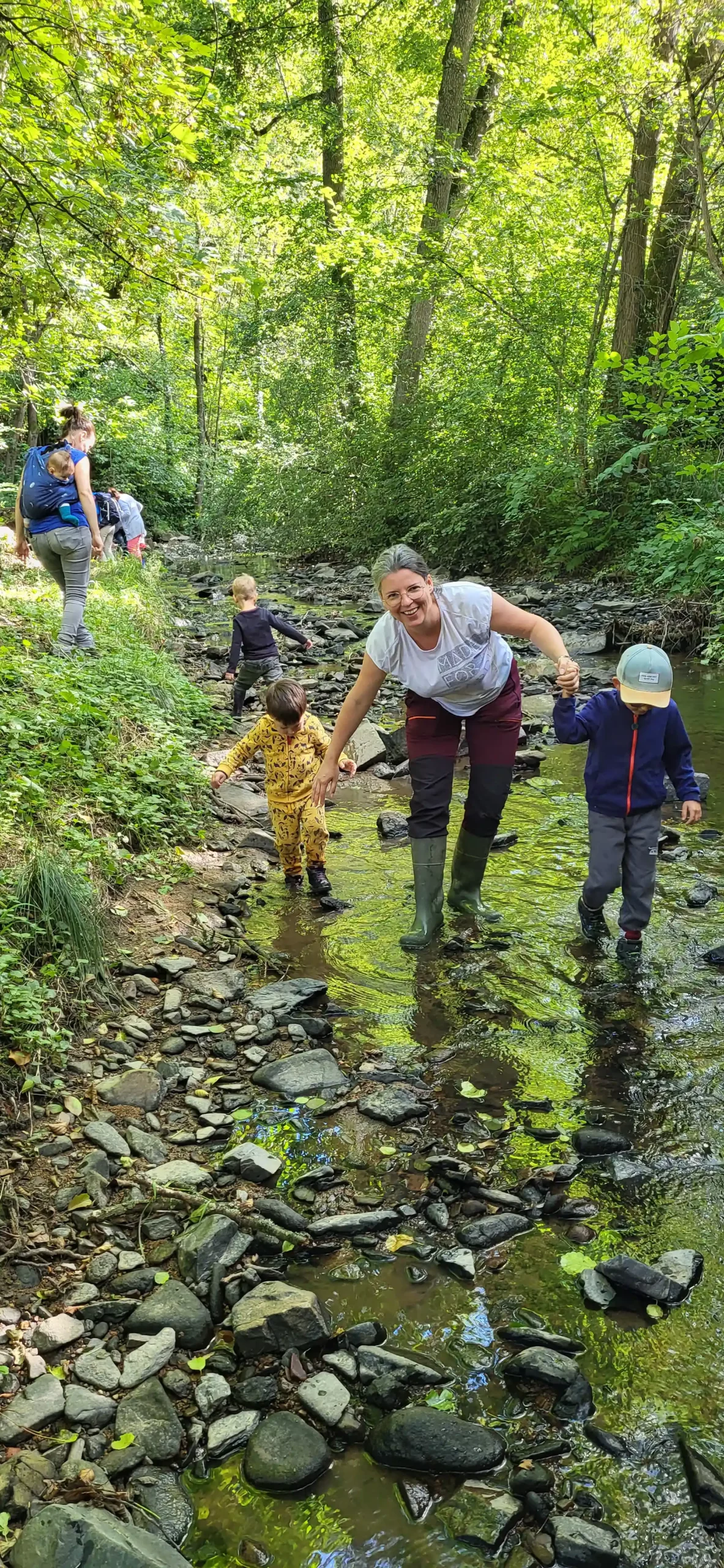 L'animatrice nature accompagne les enfants pour marcher dans la rivière